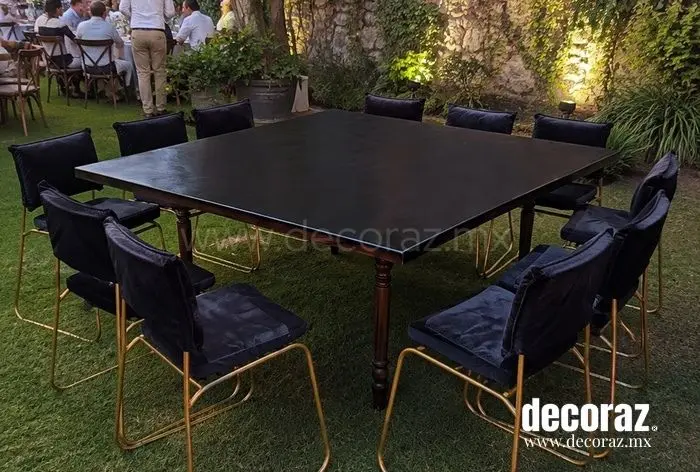 Mesa de madera negra con sillas metálicas doradas y cojines negros para evento elegante